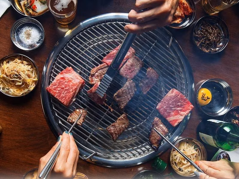 Diners cooking cuts of beef on a tabletop Korean barbecue grill